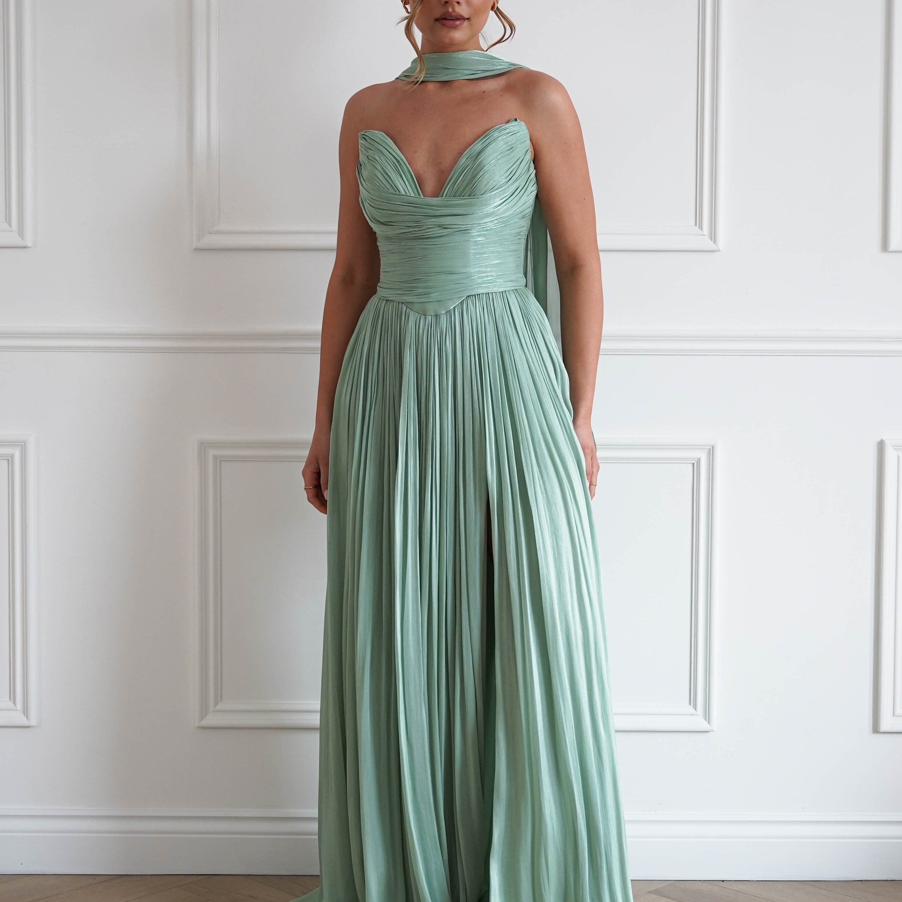 Woman wearing a sage green pleated maxi gown with a strapless sweetheart neckline, ruched bodice, flowing floor-length skirt, and matching neck scarf, perfect for prom, black-tie events, bridesmaid parties, and formal occasions.