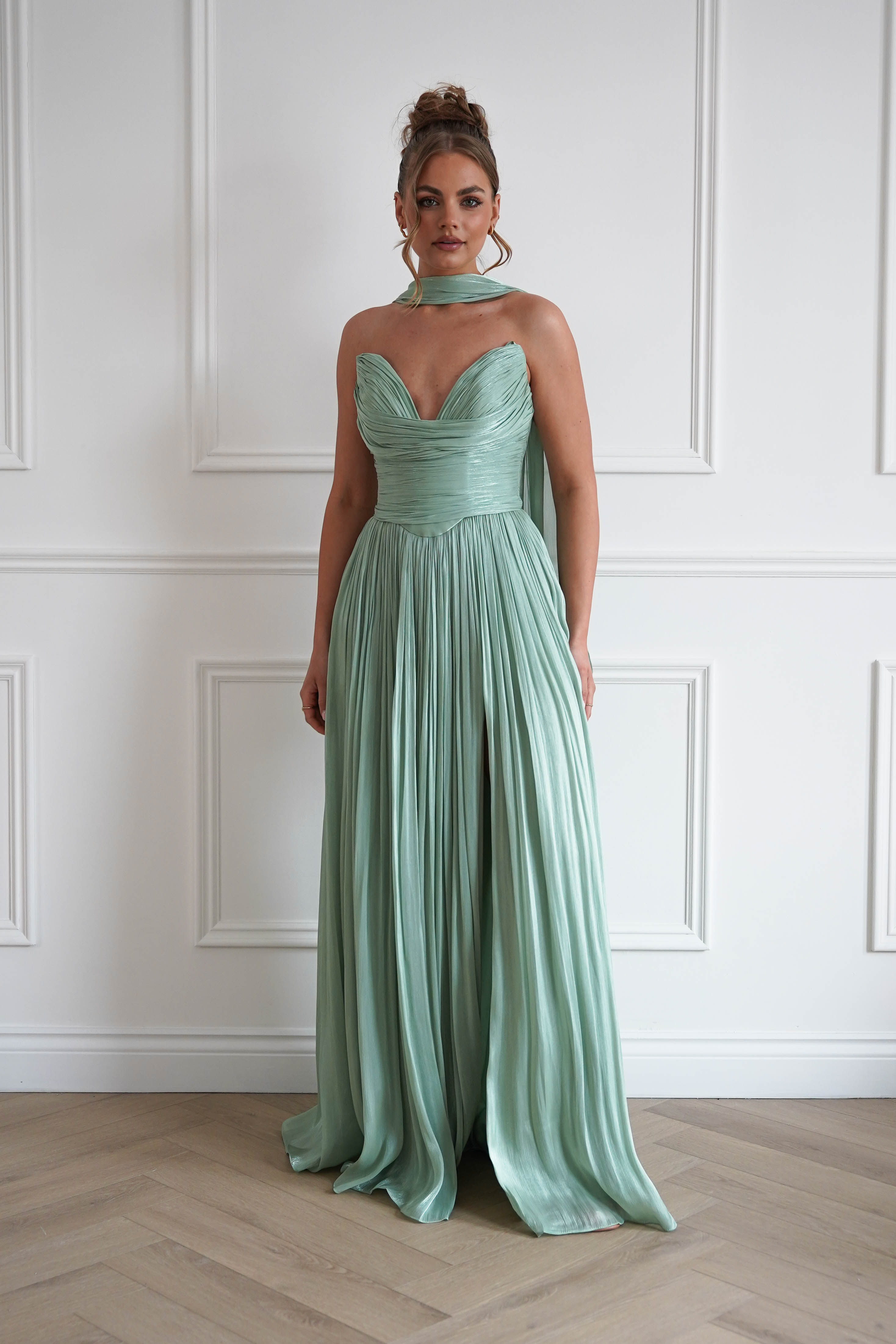 Woman wearing a sage green pleated maxi gown with a strapless sweetheart neckline, ruched bodice, flowing floor-length skirt, and matching neck scarf, perfect for prom, black-tie events, bridesmaid parties, and formal occasions.