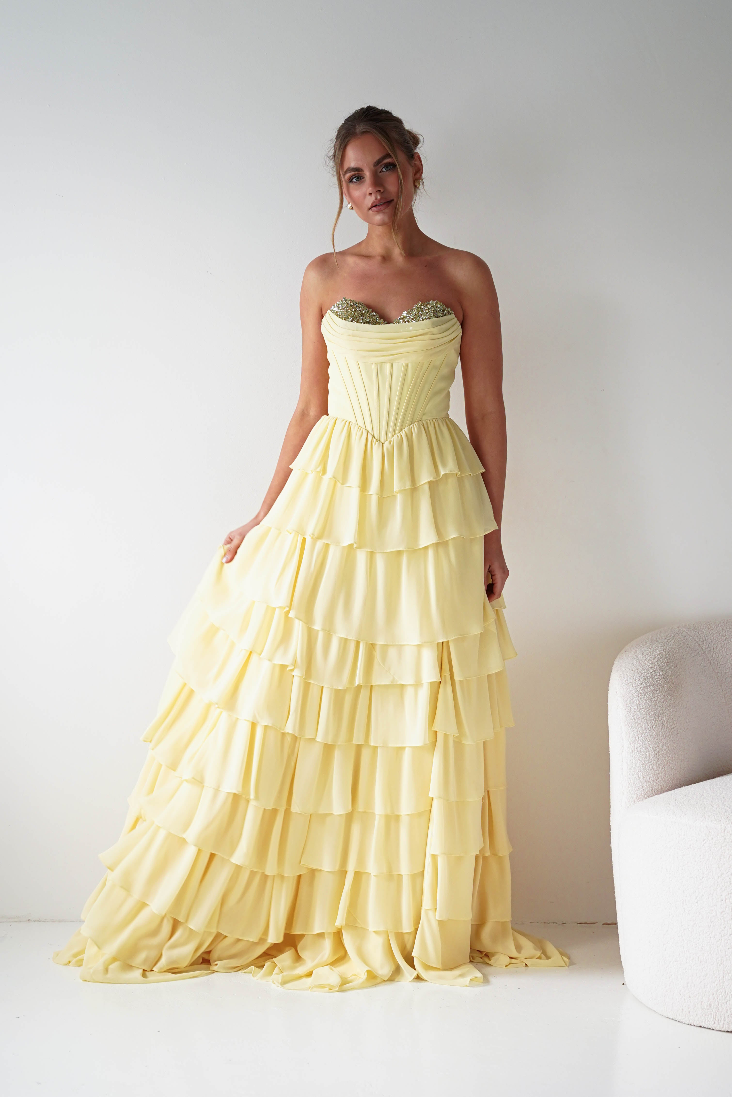 Woman wearing a yellow strapless gown with ruffled layers against a white background