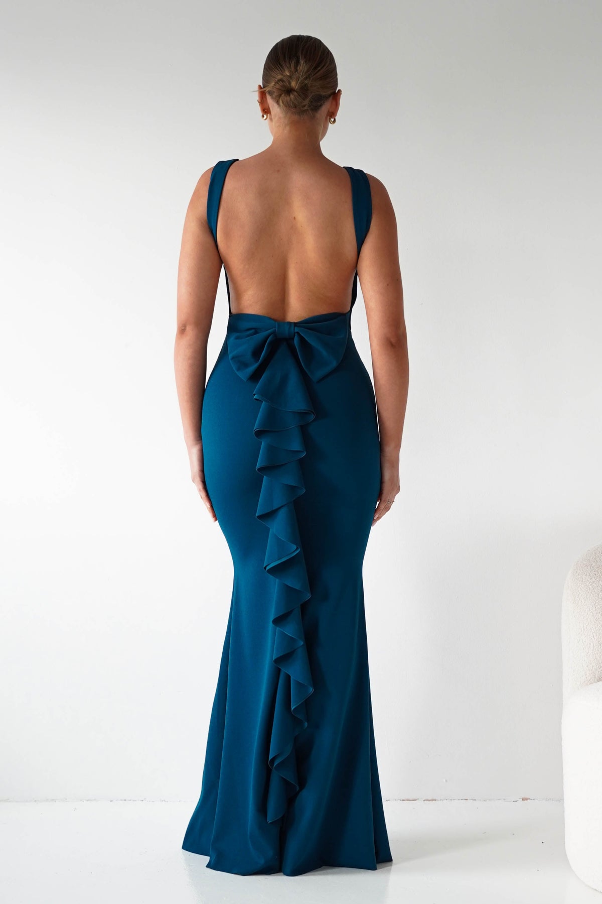 Woman wearing a teal evening gown with ruffled details on a white background