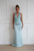 Woman wearing a mint green bodycon halterneck maxi dress with a plunging V-neckline, ruched bodice detailing, and a fitted satin-look floor-length silhouette, ideal for weddings, bridesmaid events, galas, and formal occasions.