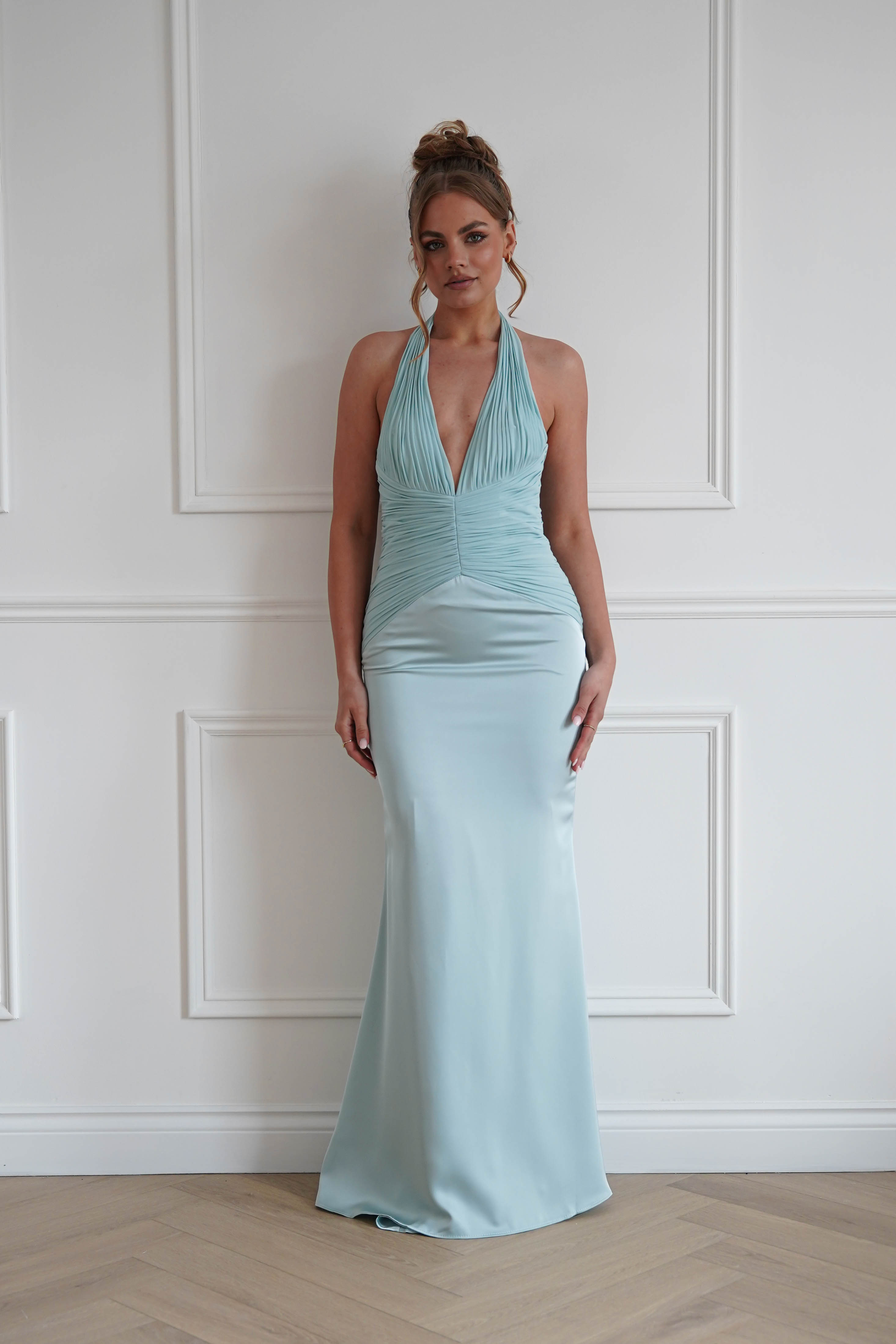 Woman wearing a mint green bodycon halterneck maxi dress with a plunging V-neckline, ruched bodice detailing, and a fitted satin-look floor-length silhouette, ideal for weddings, bridesmaid events, galas, and formal occasions.