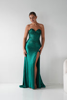Woman wearing a green strapless gown with a high slit on a white background
