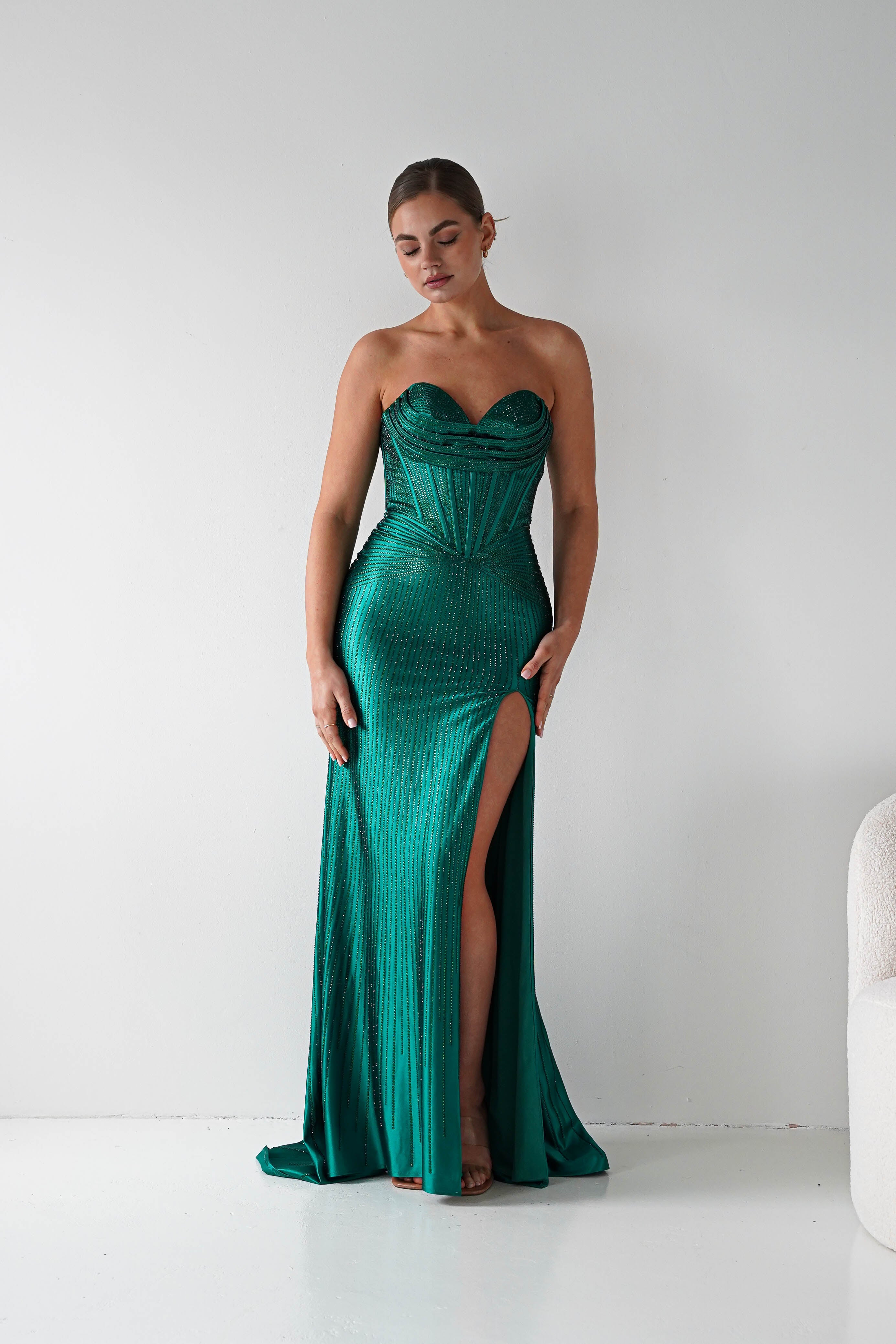 Woman wearing a green strapless gown with a high slit on a white background
