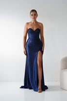 Woman wearing a strapless blue evening gown with a slit on a white background