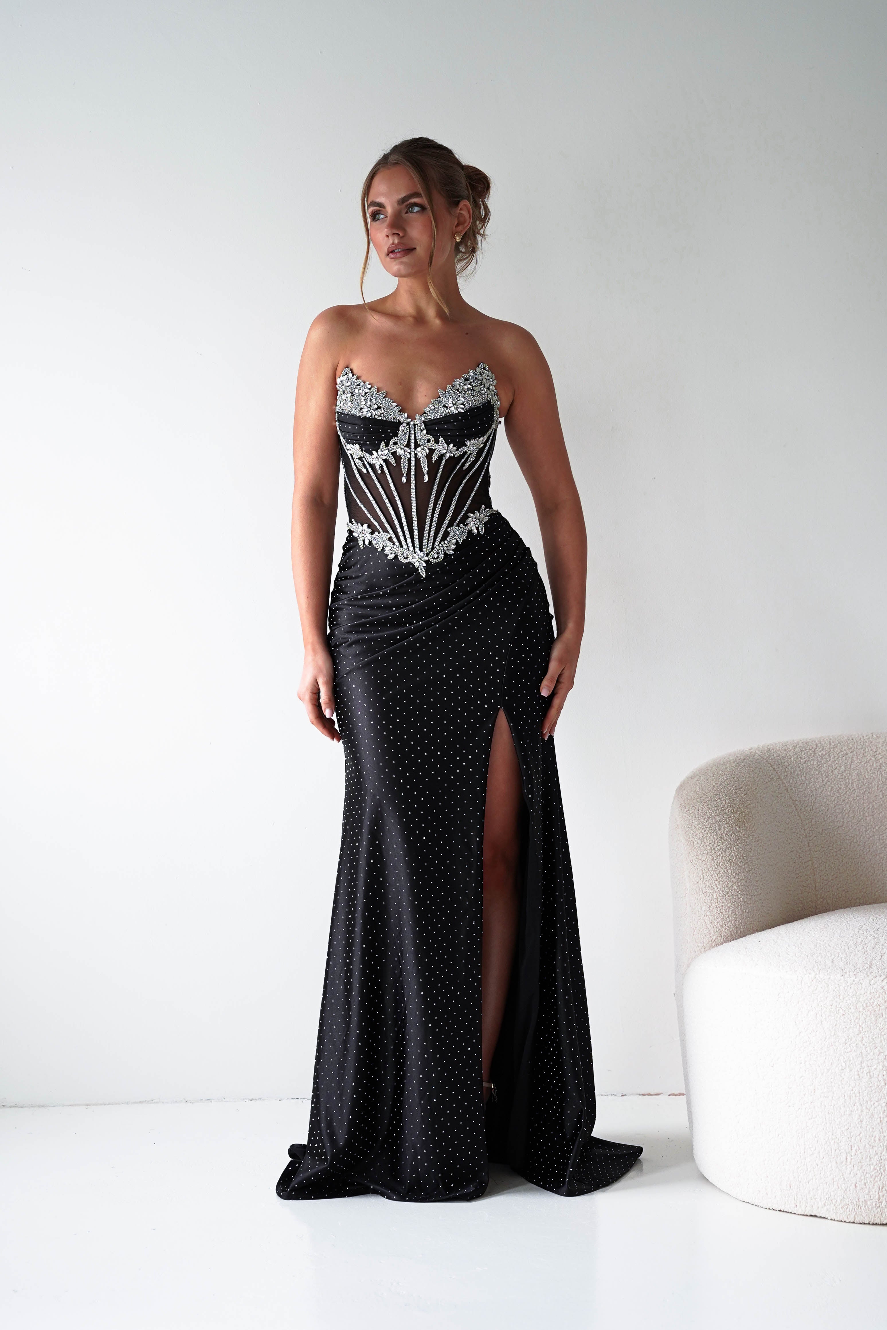 Woman wearing a black polka dot evening gown with silver detailing on a white background