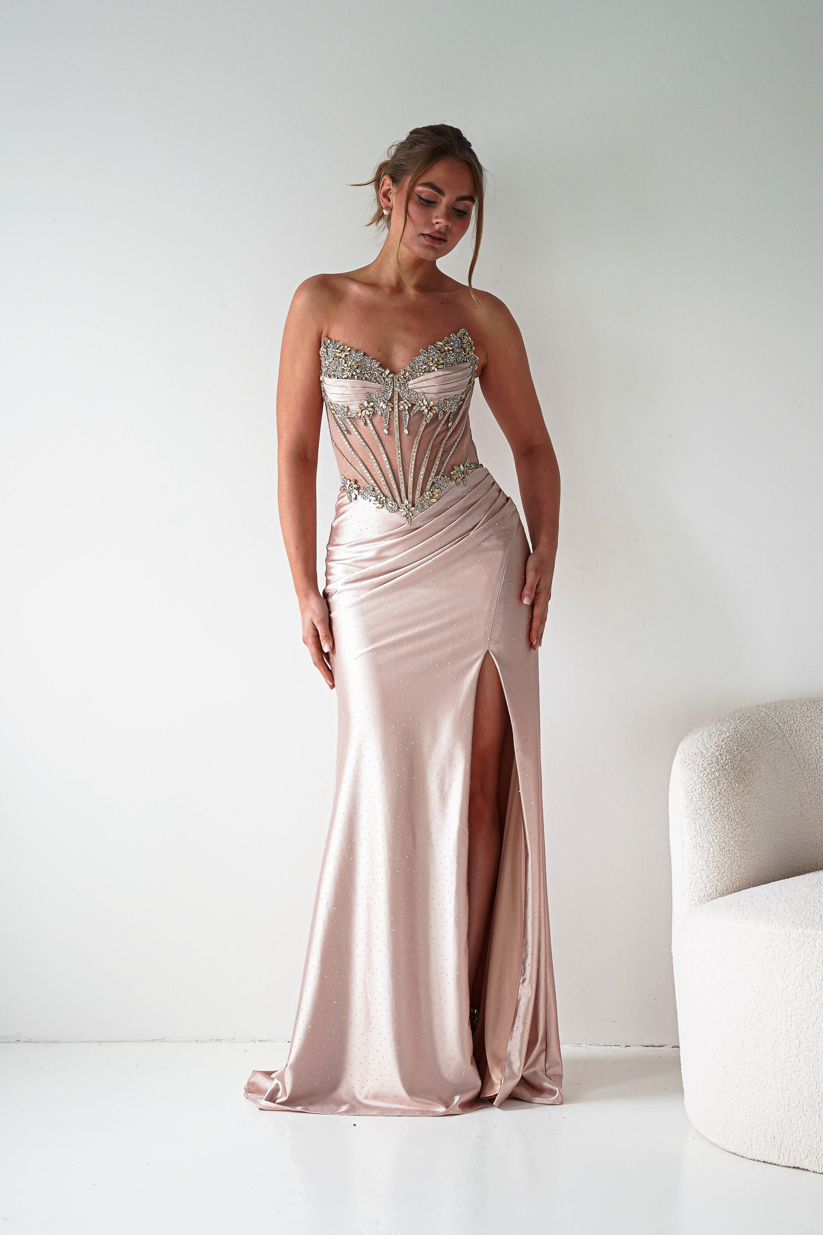 Woman wearing a strapless, embellished gown with a high slit on a white background