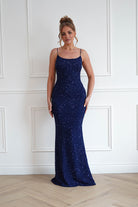 Woman wearing a navy blue sequin bodycon maxi gown with delicate spaghetti straps, a fitted silhouette, and floor-length hem, perfect for prom, gala events, black-tie occasions, and evening celebrations.