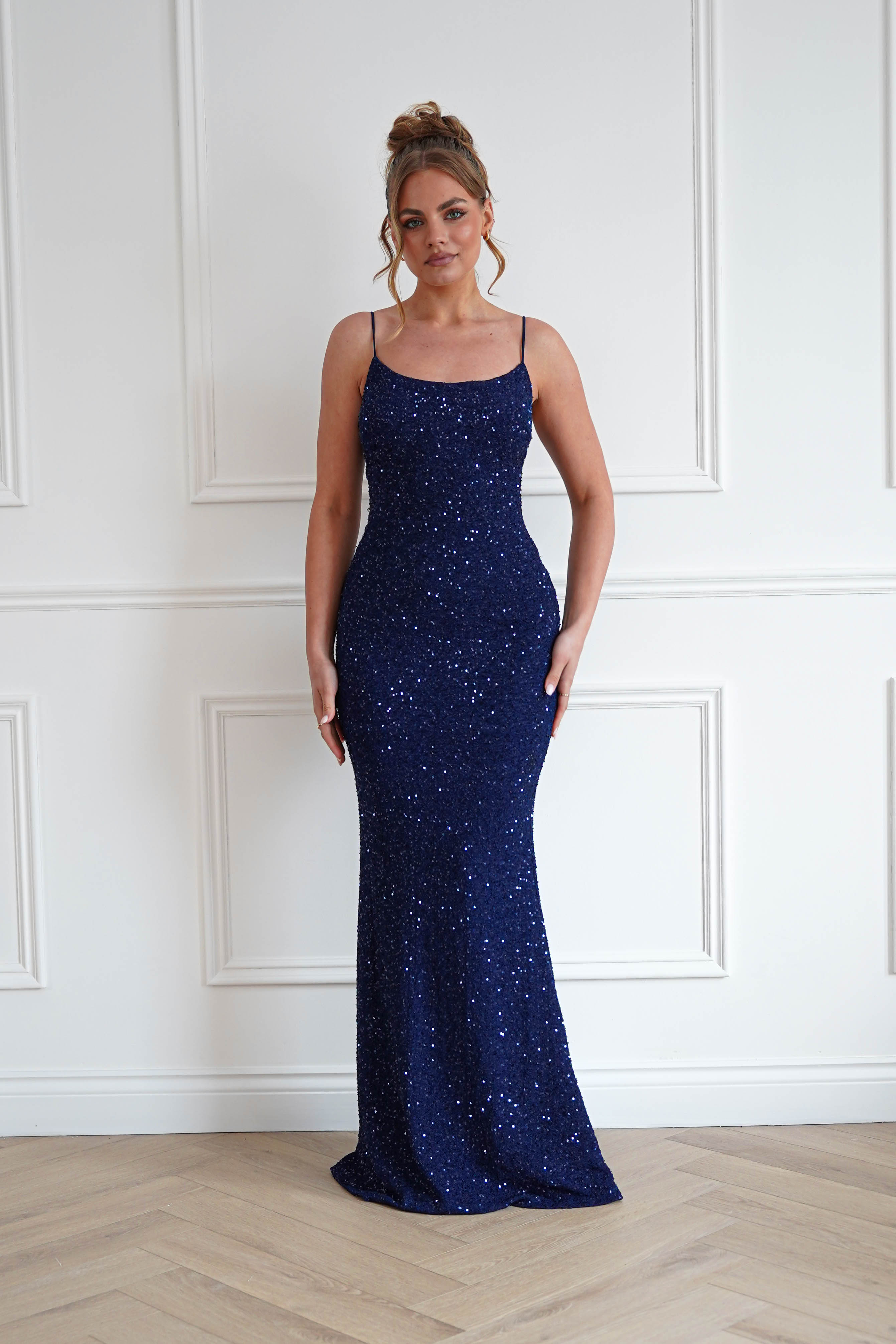 Woman wearing a navy blue sequin bodycon maxi gown with delicate spaghetti straps, a fitted silhouette, and floor-length hem, perfect for prom, gala events, black-tie occasions, and evening celebrations.