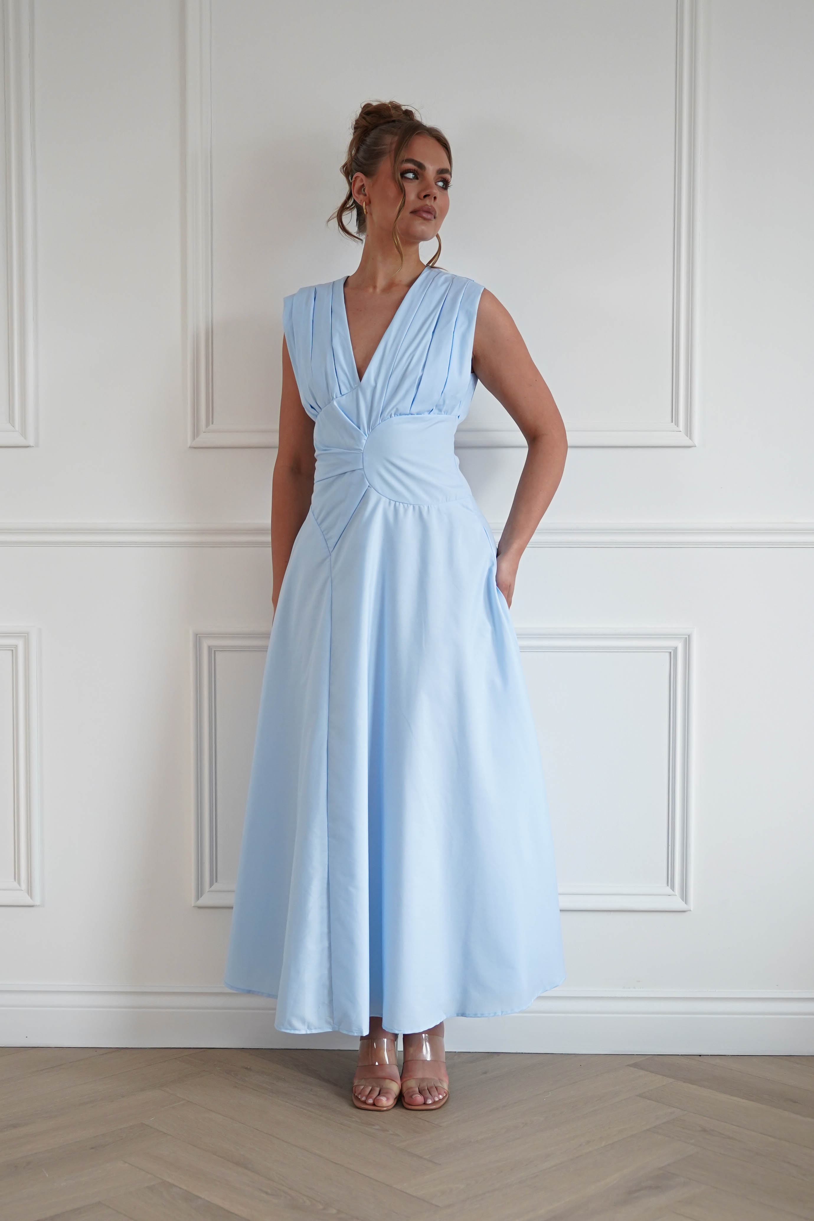 Woman wearing a baby blue midi dress with a sleeveless V-neckline, twist waist detailing, and a flowing A-line skirt, perfect for weddings, garden parties, baby showers, and special occasions.