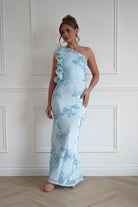 Woman wearing a light blue one-shoulder bodycon maxi dress with floral embroidered detailing and statement ruffle shoulder accents, ideal for weddings, races, and formal occasions.