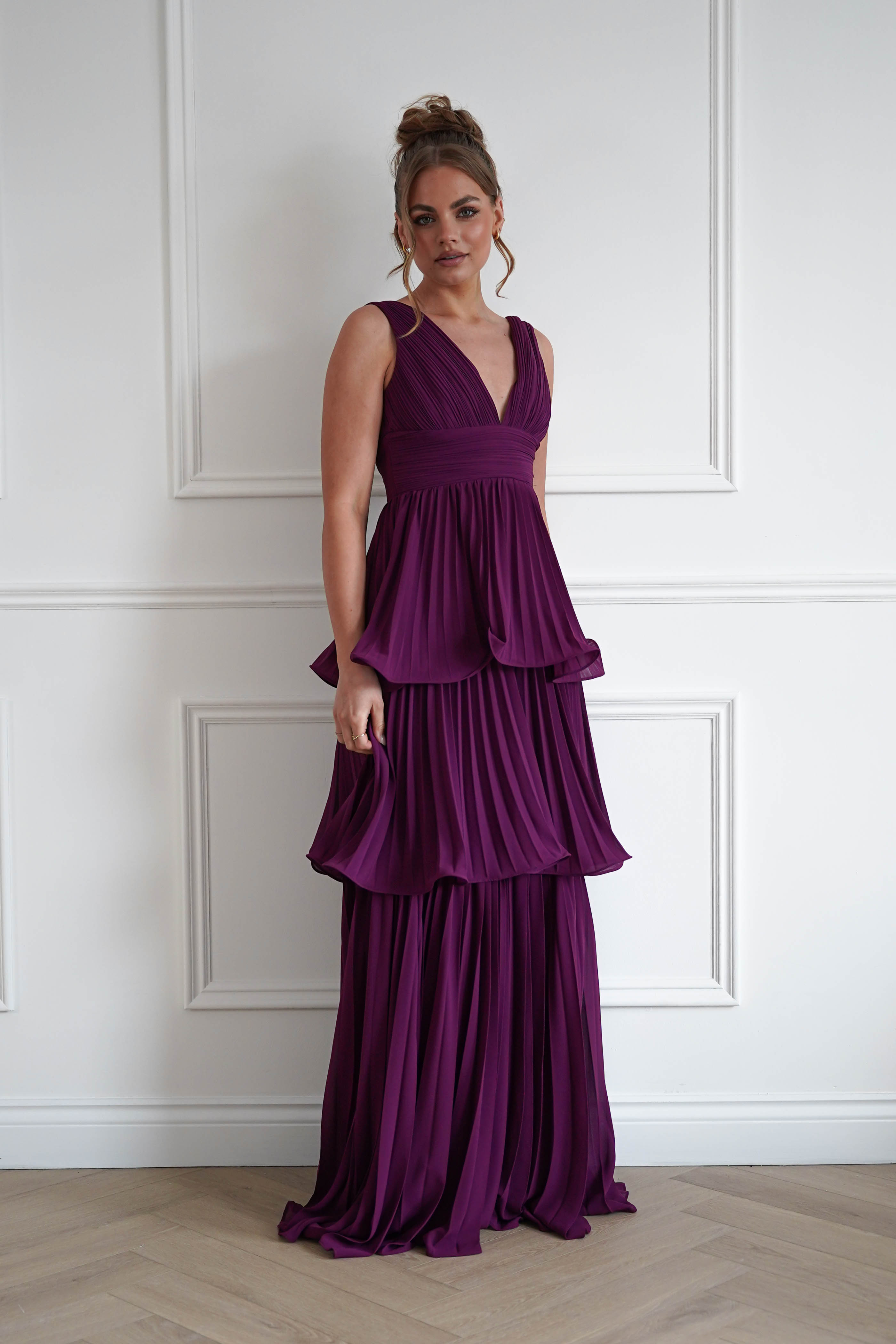 Woman wearing the Vina tiered pleated layered maxi dress in plum with a deep V-neckline, flowing pleated tiers, and floor-length elegant silhouette.